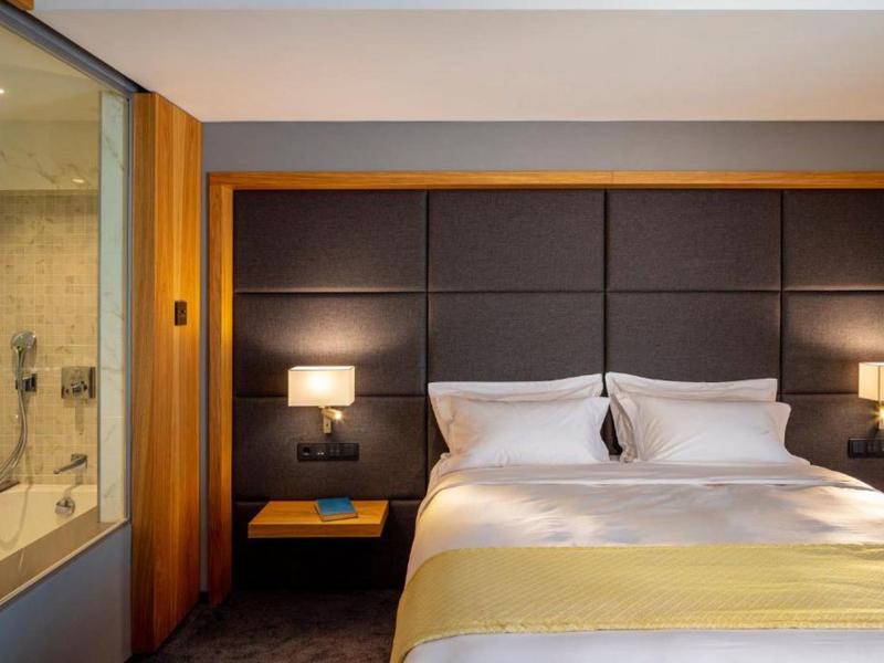 Modern hotel room with large bed, dark headboard, and two bedside lamps.