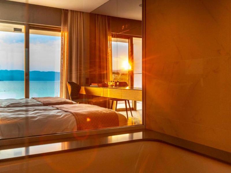 Modern hotel room with large windows and ocean view at sunset.