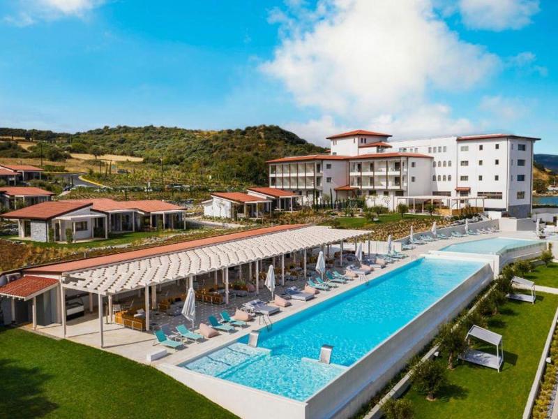 Hotel with a large outdoor pool, sun loungers, and hills in the background on a sunny day.