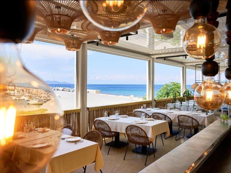Bright restaurant with large windows and sea view in daylight.