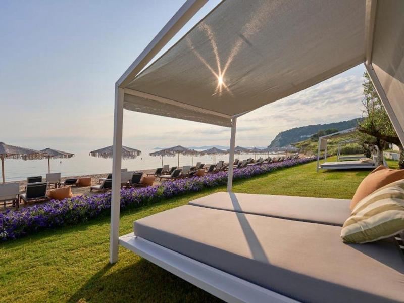 Large sunbed with pillows under a canopy overlooking loungers and the sea.