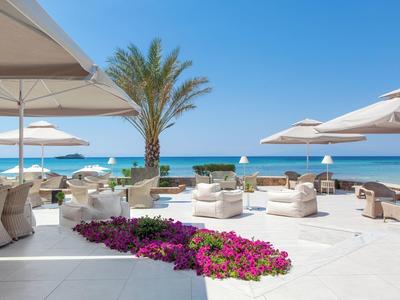 Luxuriöse Strandterrasse mit weißen Sitzmöbeln, Sonnenschirmen und Blick aufs blaue Meer.