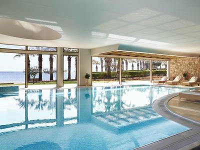 Piscina interna con grandi finestre che si affacciano su palme e spiaggia alla luce del giorno.