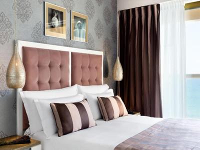 Una camera moderna con un grande letto, cuscini decorativi e tende scure.