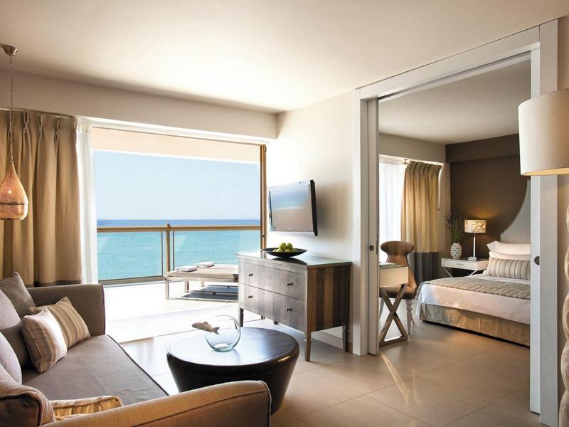 Camera d'hotel luminosa con vista mare, divano moderno e camera da letto adiacente.