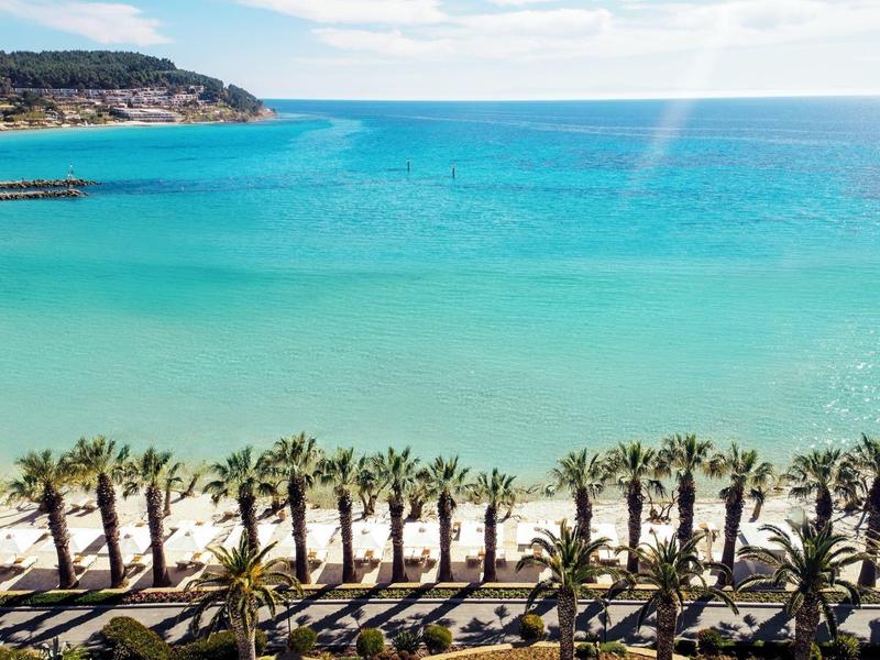 Vista di una spiaggia con acqua turchese e una fila di palme lungo la riva.