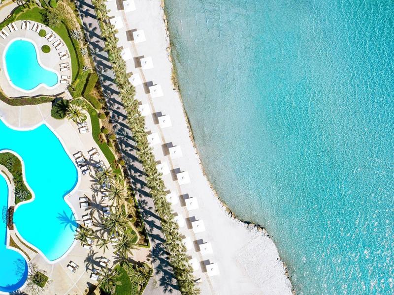 Veduta aerea di una spiaggia con mare turchese e area piscina adiacente.