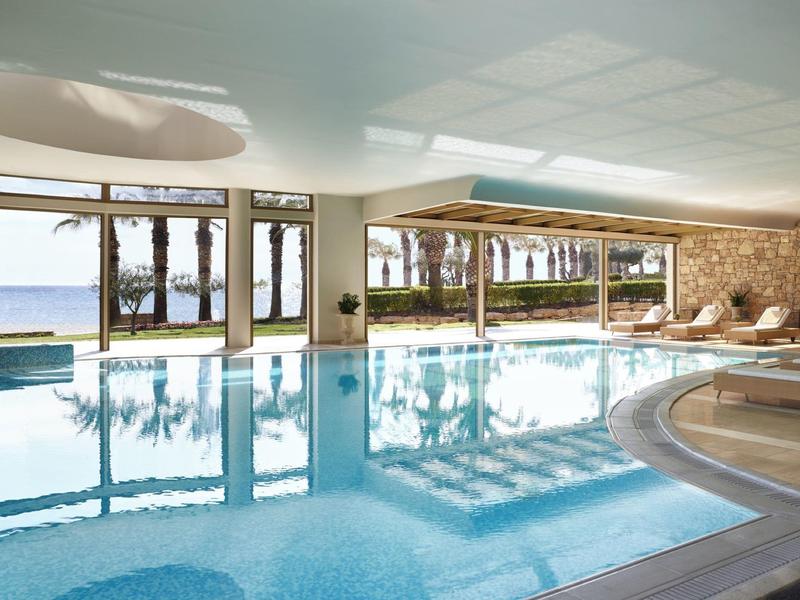 Piscina interna con grandi finestre che si affacciano su palme e spiaggia alla luce del giorno.