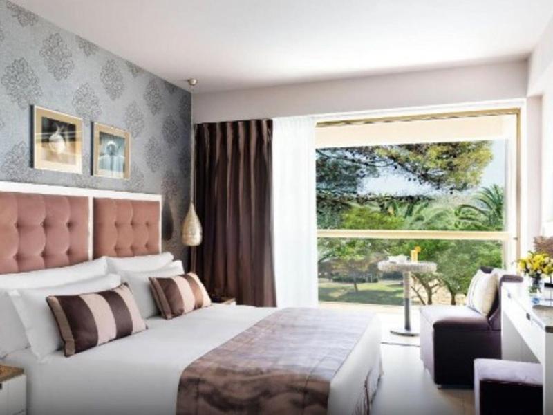 Camera d'hotel moderna con letto grande, cuscini pastello e finestra panoramica con vista sul verde.