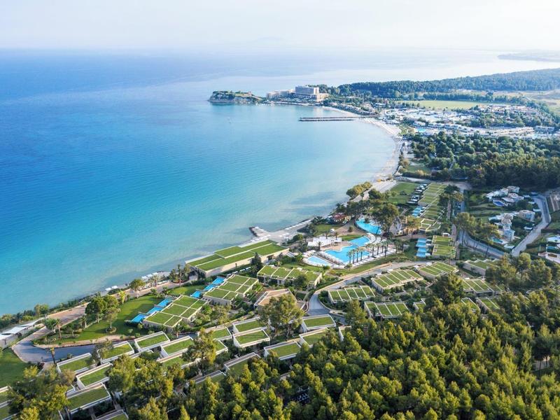 Letecký pohled na přímořské město s modrým mořem, plážemi a zelenými lesy v popředí.