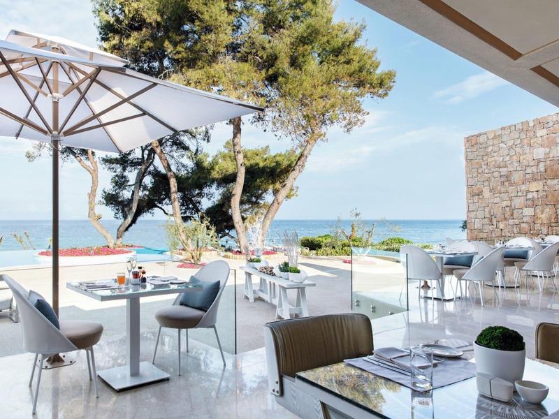 Moderní terasa s židlemi, stoly a slunečníky s výhledem na moře.