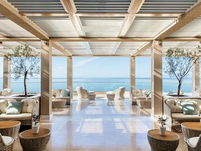 Moderner, offener Lounge-Bereich mit Blick auf Meer und Terrasse, helle Einrichtung und Pflanzen.