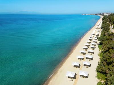 Spiaggia di sabbia bianca con file di ombrelloni accanto al mare turchese e alla vegetazione verde.
