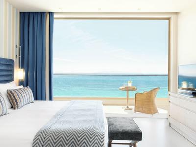 Camera d'hotel moderna con vista mare, letto grande e balcone con sedie.