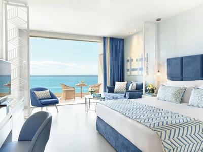 Camera d'hotel moderna con vista mare, letto matrimoniale e area salotto sul balcone.