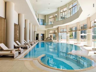 Piscina interna luminosa con finestre ad arco, lettini e arredamento beige.