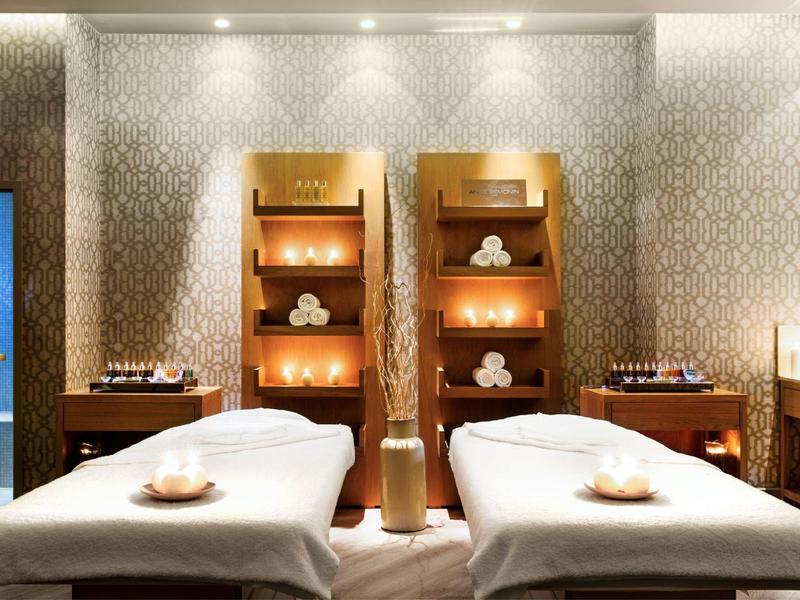 Due lettini per massaggi in una spa accogliente con illuminazione calda e scaffali pieni di asciugamani.