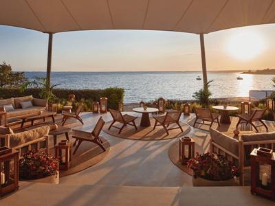 Espace assis ouvert avec mobilier en bois donnant sur la mer au coucher du soleil.