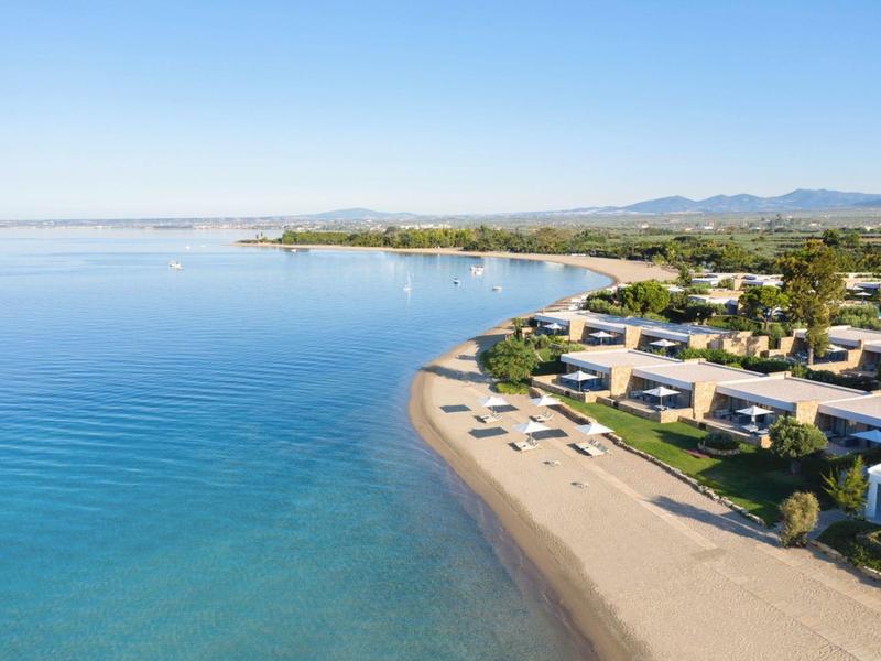 Ein ruhiger Sandstrand mit Sonnenliegen neben modernen Strandhäusern und klarem, blauem Wasser.