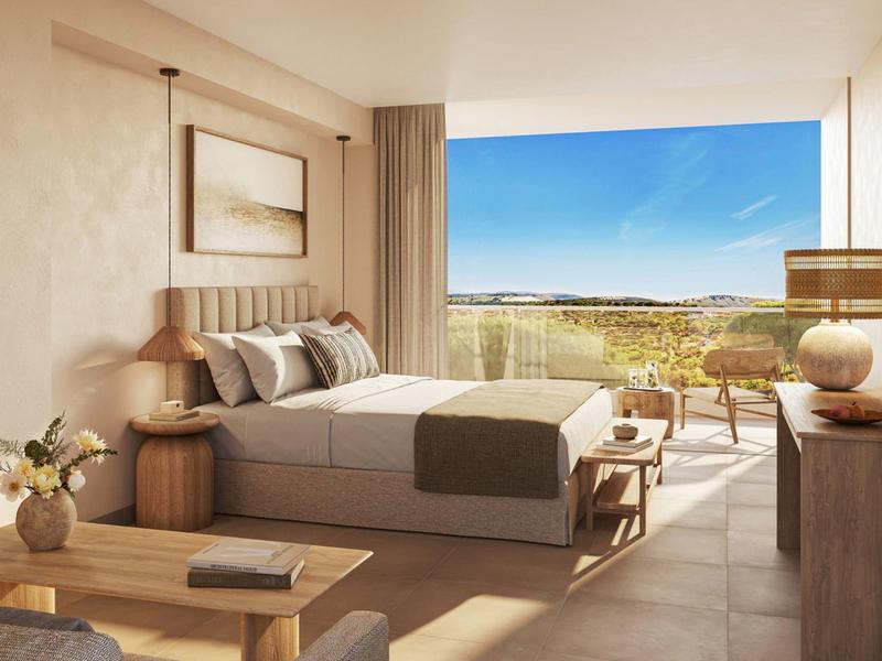 Helles Hotelzimmer mit großem Bett und Balkon mit Aussicht auf Landschaft und blauen Himmel.