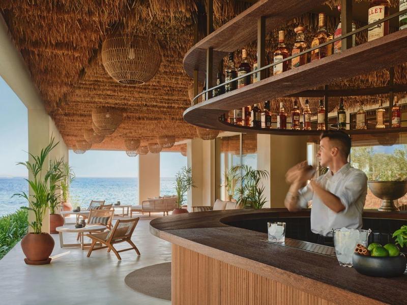 Offene Bar mit Blick auf das Meer und entspannte Sitzgelegenheiten unter einem Strohdeckendach.