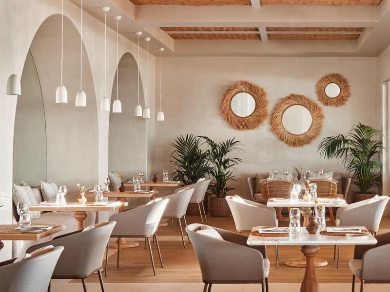 Helles Restaurant mit weißen Stühlen, Holztischen und dekorativen Wandspiegeln in Rundform.