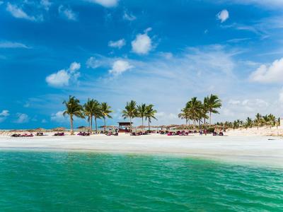 Pláž s bílým pískem, palmami a čistou tyrkysovou vodou pod modrou oblohou.