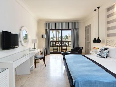 Světelný hotelový pokoj s manželskou postelí, psacím stolem, TV a balkonem s výhledem na moře.