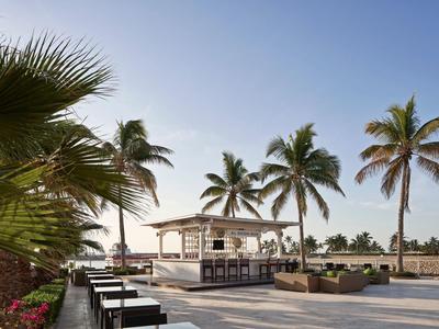 Venkovní bar se stoličkami obklopený palmami pod jasnou slunečnou oblohou.