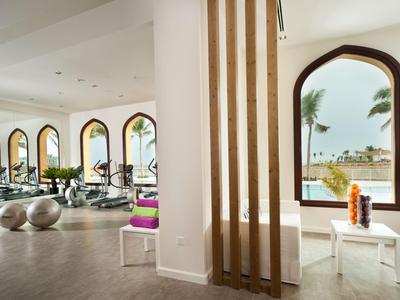 Modern gym with views of the sea and palm trees through large windows.