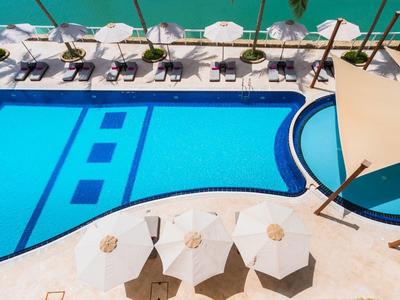 Pohled na modrý bazén s bílými lehátky a slunečníky vedle čisté vody.