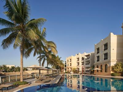 Hotel with pool and palm trees under clear blue sky.