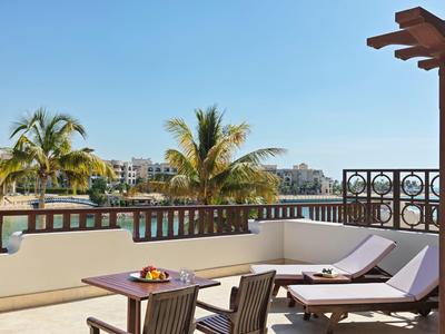 Terasa se dvěma lehátky, stolem a palmami s výhledem na budovy za jasné oblohy.