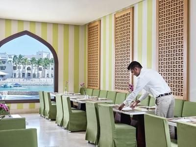 Restaurace se zelenými židlemi, zdobenými stěnami a výhledem na bazén a palmy.