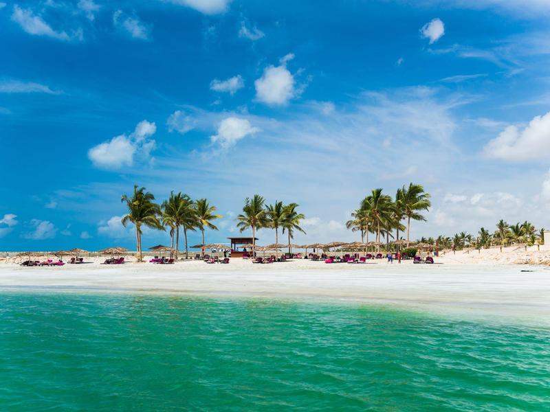 Pláž s bílým pískem, palmami a čistou tyrkysovou vodou pod modrou oblohou.