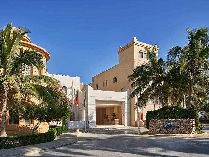 Vstupní prostor hotelu s palmami a jasnou modrou oblohou.