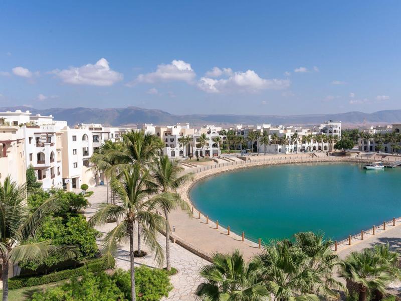 Pobřežní hotel s privátní pláží, palmami a tyrkysovou vodou pod slunečnou oblohou.