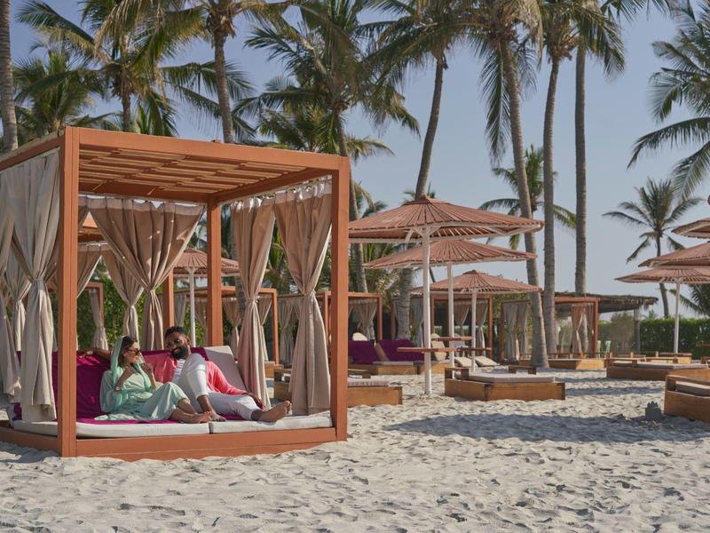 Pláž s dřevěnými altány, palmami a lehátky pod slunečníky u moře.