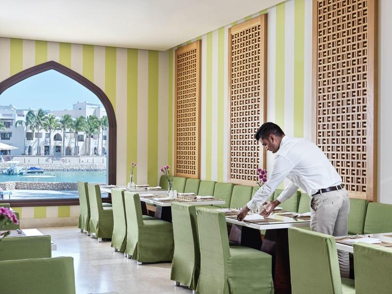 Restaurace se zelenými židlemi, zdobenými stěnami a výhledem na bazén a palmy.