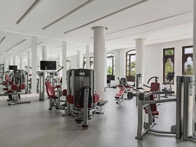 Moderner Fitnessraum mit verschiedenen Trainingsgeräten und großen Fenstern in einem Hotel.
