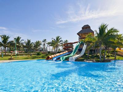 Wasserpark mit großen Rutschen, klarem blauen Pool und Palmen bei sonnigem Himmel.