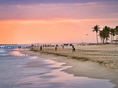 Strand mit Palmen und Menschen bei Sonnenuntergang mit ruhigem Meer