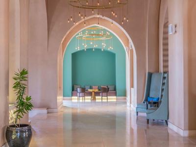 Ein heller Gang mit hohen Bögen, Pflanzen und einem Sitzbereich in der Ferne mit blauer Wand.