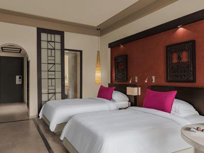 Modernes Schlafzimmer mit zwei Einzelbetten, weißen Bettdecken, pinken Kissen und dekorativer Wandkunst.