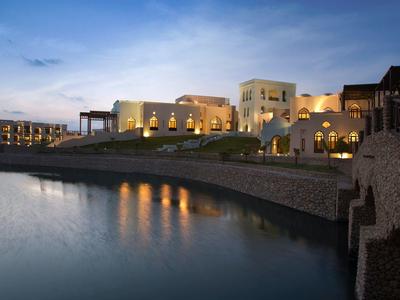 Elegante Gebäude mit warmem Licht am Ufer eines ruhigen Sees bei Abenddämmerung.