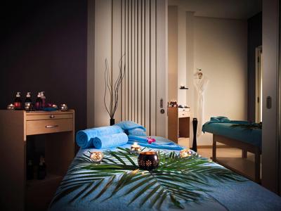 Ein ruhiger, gedämpft beleuchteter Massageraum mit blauem Bett und pflanzlicher Dekoration.