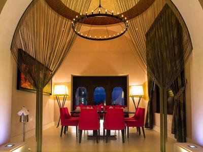 Eleganter Speiseraum mit rotem Stuhlset, hohen Decken, samtigen goldfarbenen Vorhängen und warmem Licht.