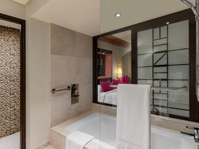 Modernes Badezimmer mit Badewanne, Handtuchhalter, großem Spiegel und Zugang zu einem Schlafzimmer.