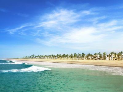 Weitläufiger Sandstrand mit Palmen unter blauem Himmel und leicht bewölkter Atmosphäre.