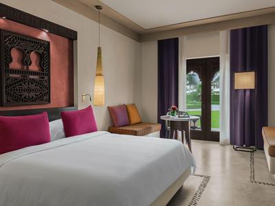 Modernes Schlafzimmer mit großem Bett, bunten Kissen, Fenster mit Vorhängen und gemütlichen Sitzbereichen.